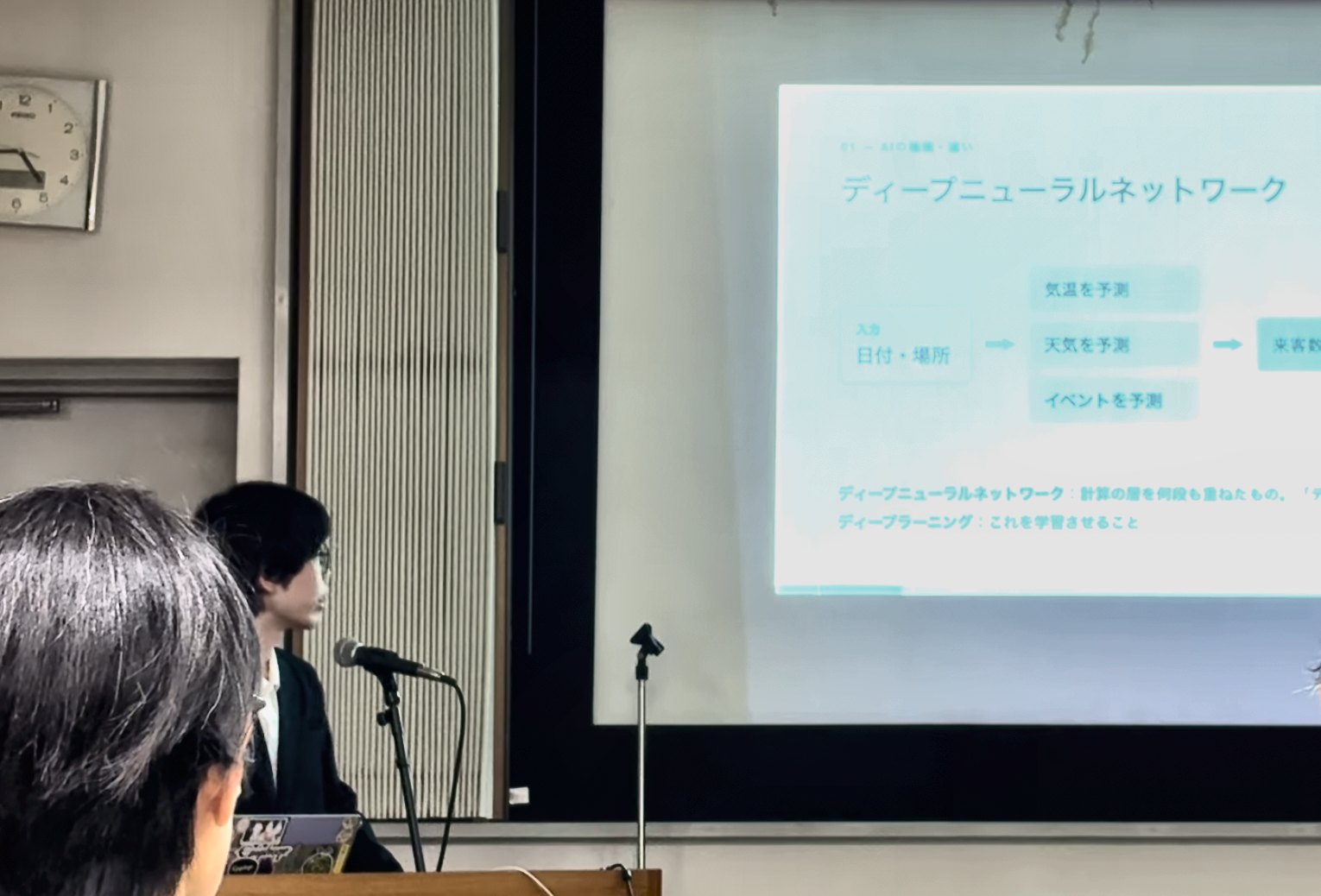 演台のマイクの前で話す講演者と、スクリーンに映った「ディープニューラルネットワーク」のスライド